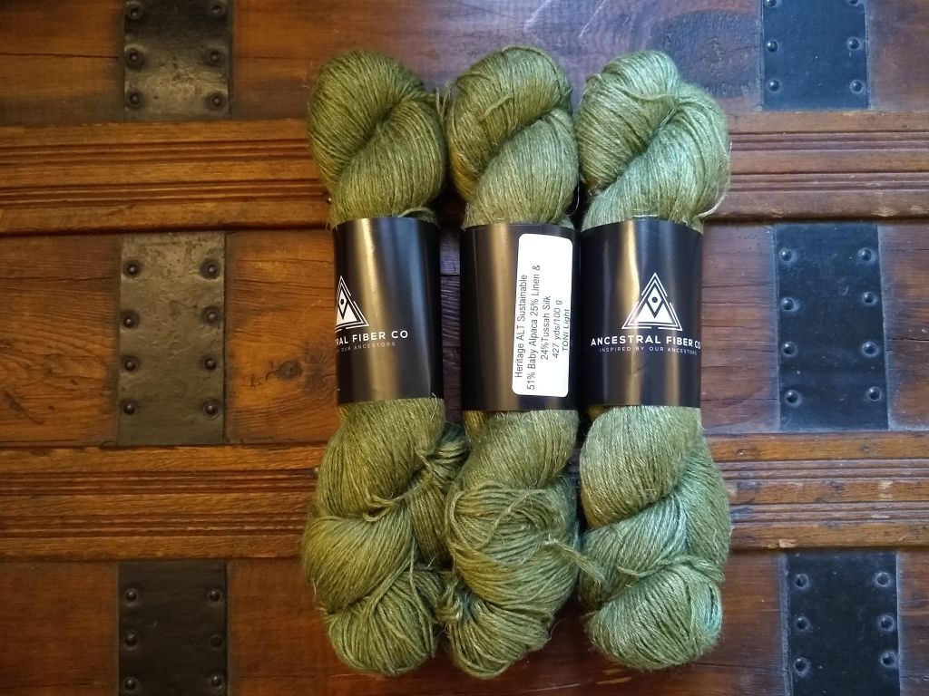 Three skeins of sage green yarn lay on an old, wooden trunk with cast iron brackets. The silk content of the yarn gives it a very pretty sheen.